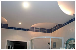 Biała łazienka z podwieszanym sufitem o nieregularnym kształcie, wykończona niebieską mozaiką, widoczny fragment kabiny prysznicowej i drzwi.